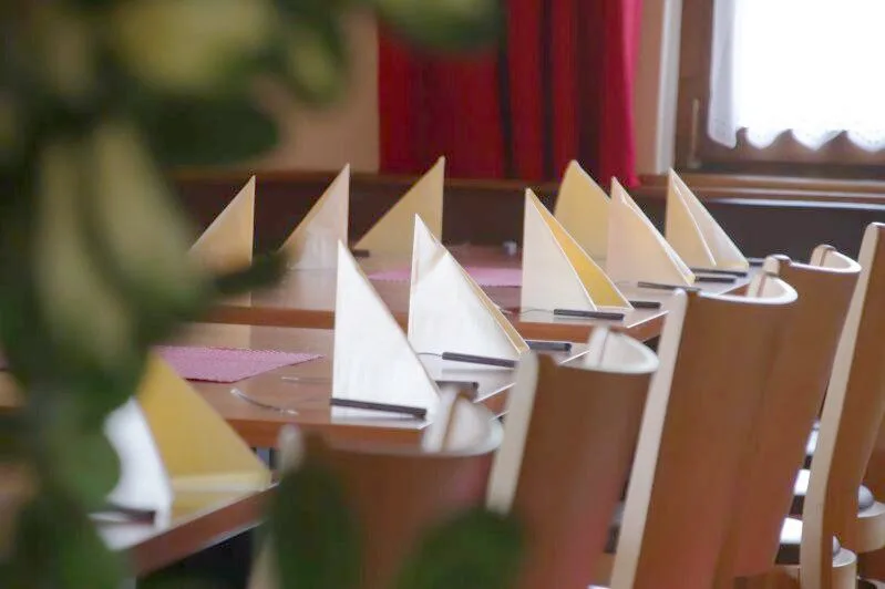 Gedeckte Tafel mit weißen Servietten vor dem roten Vorhang der Gaststube