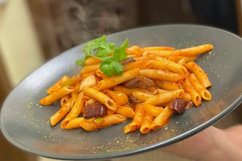 Penne in Tomatensauce mit Oliven, vom Personal zum Tisch getragen