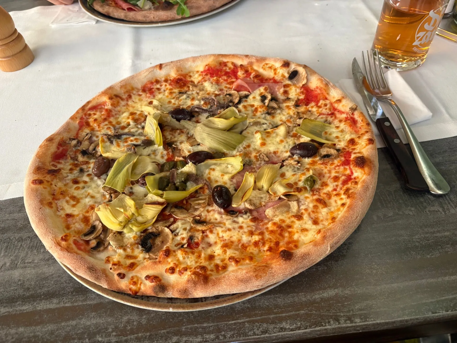 Pizza mit Artischocken, Champignons und Oliven auf dem Tisch im Lokal