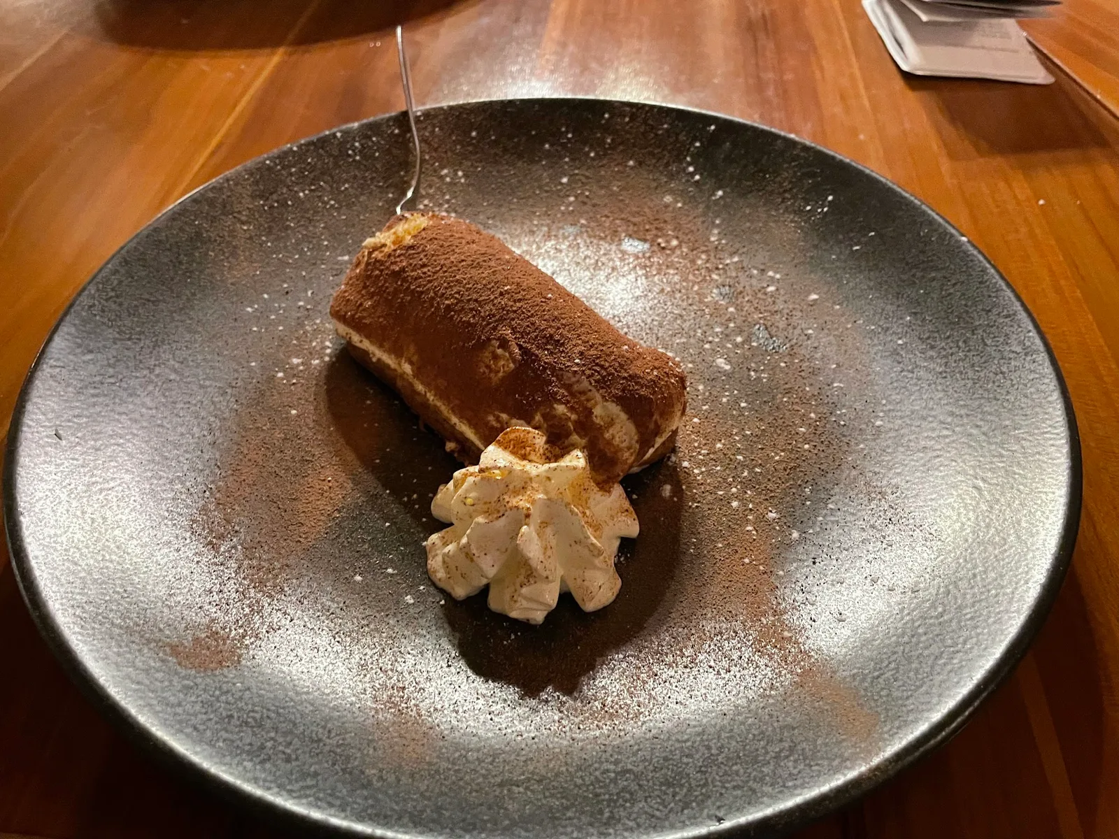 Tiramisu mit Schlagobers und Kakao auf einem dunklen Teller