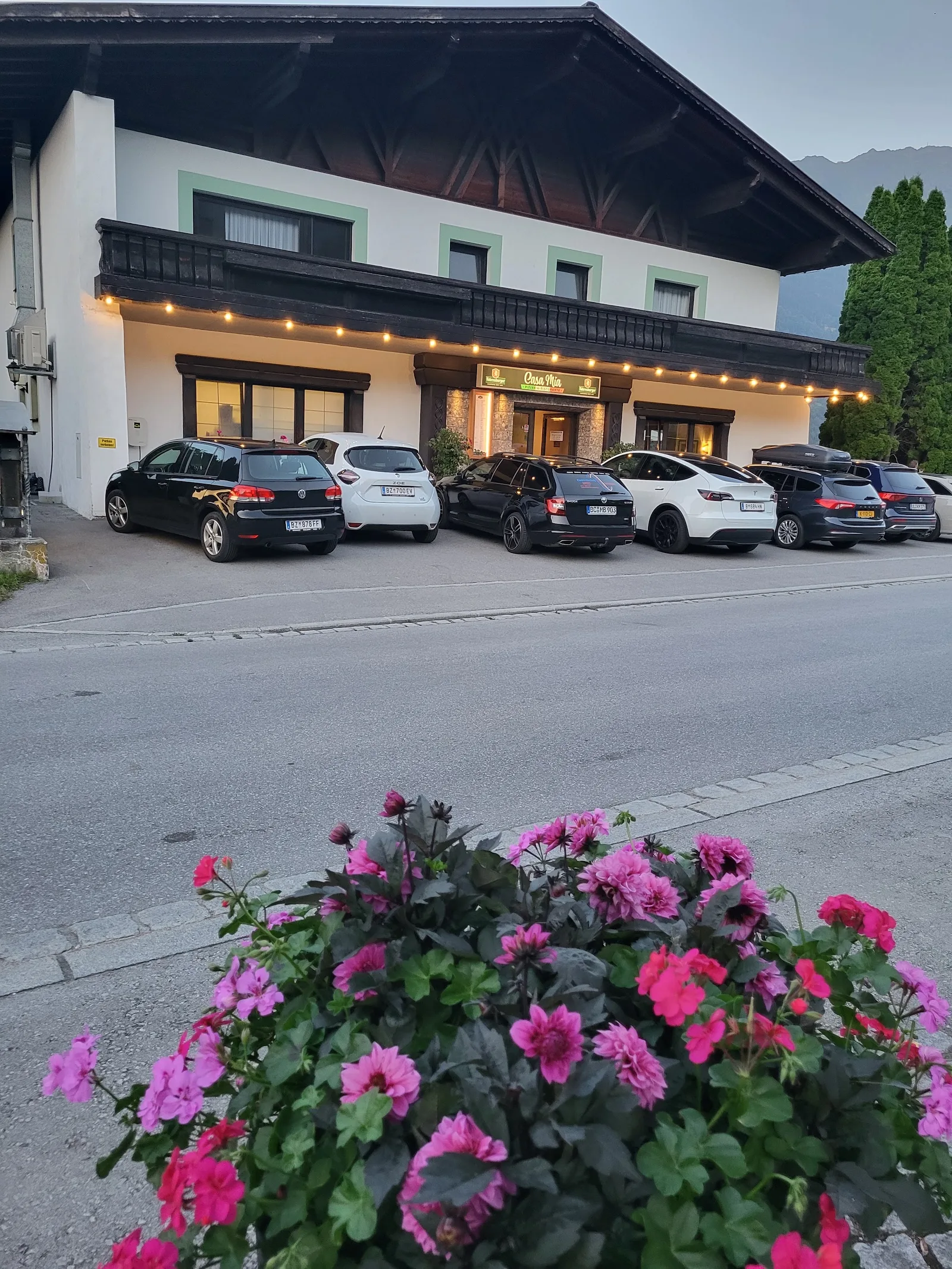Das Haus der Pizzeria am Abend, mit Lichterkette über dem Eingang und Blumen davor